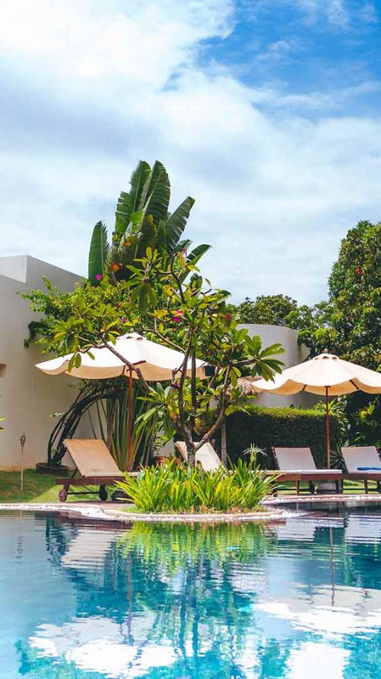 a pool surrounded by lush green trees and a lounge chair at The Discovery Park Life Apartments